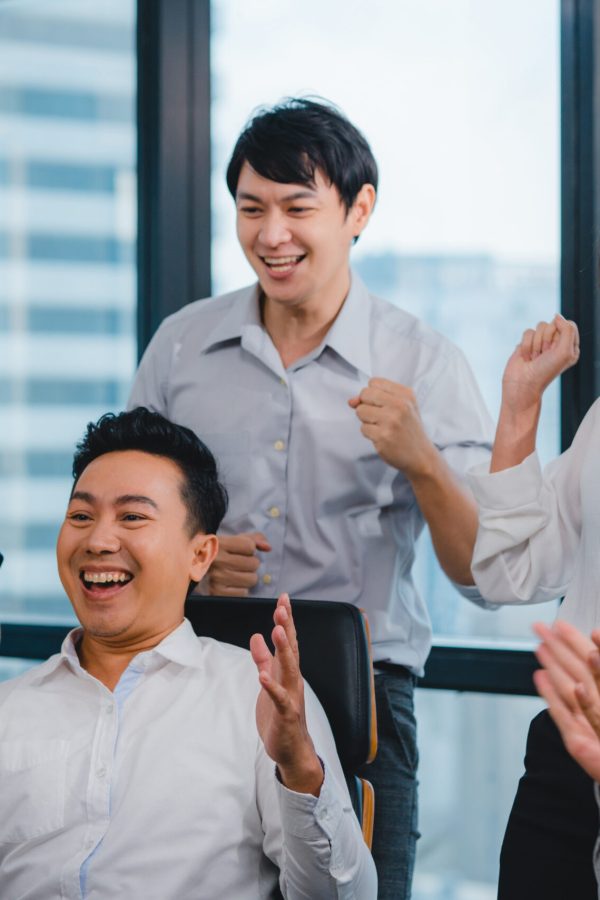Millennial group of young businesspeople Asia businessman and businesswoman celebrate giving five after dealing feeling happy and signing contract or agreement at meeting room in small modern office.